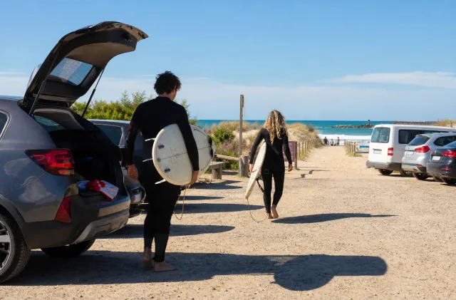 Surfeurs portant des planches depuis un parking de Santocha vers l'océan.