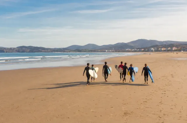 Groupe d'école de surf traversant la Grande Plage d'Hendaye avec la longue baie et les vagues douces devant.