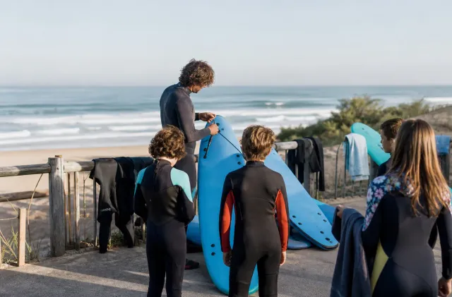 Groupe d'école de surf à Anglet préparant des planches en mousse près des dunes avec les vagues derrière.