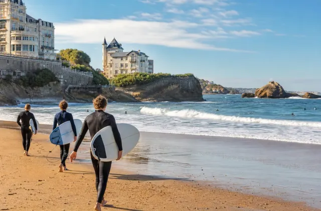 Surfeurs portant leurs planches vers l'eau sur une plage de Biarritz sous les falaises de la Côte basque.