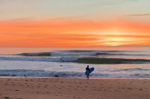 Vagues propres sur un beach break d'Anglet au coucher du soleil avec un surfeur sur le sable.