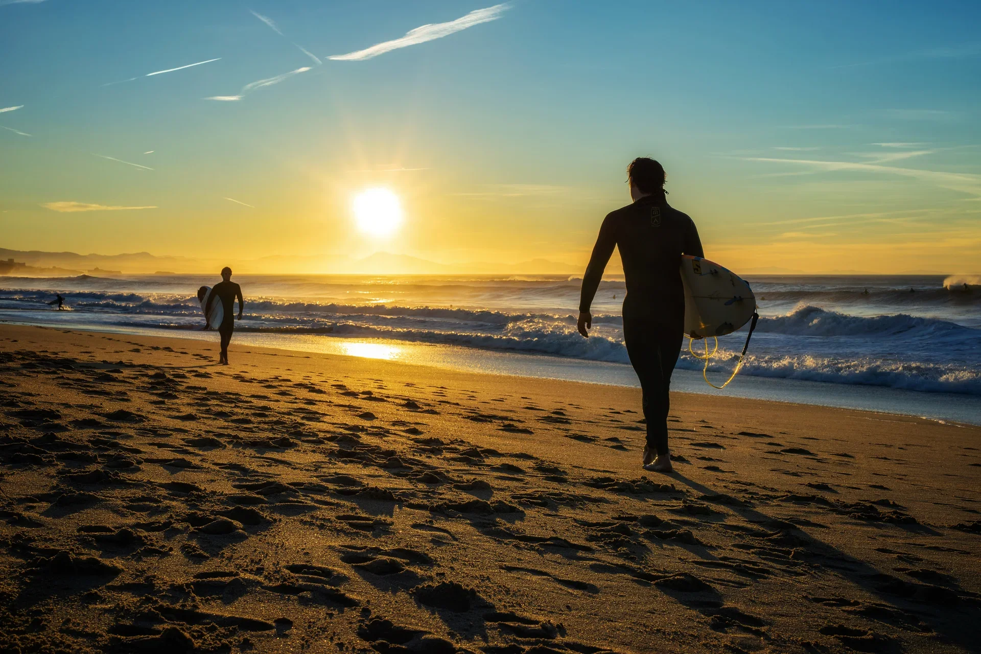 Surfeurs marchant dans la lumière dorée sur une plage d'Anglet au lever du soleil